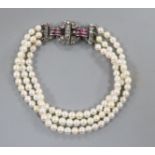 A triple strand cultured pearl bracelet with ruby and diamond set white metal clasp, 17cm.