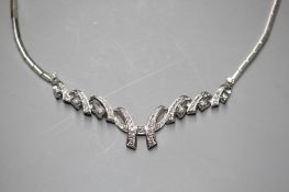 A modern 750 white metal and diamond set open scroll necklace, set with graduated round brilliant