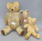 A gold plush teddy bear with plastic eyes, black stitched snout and worn brown leather pads,