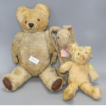 A gold plush teddy bear with plastic eyes, black stitched snout and worn brown leather pads,