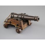 An early 20th century bronze model of a Naval cannon, on wooden trunnion base, length 25cm