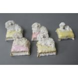 Five Staffordshire porcelain toy figures of four poodles and a King Charles spaniel recumbent on a