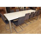 A modern large opaque glass and metal dining table and a set of twelve cloth-upholstered metal