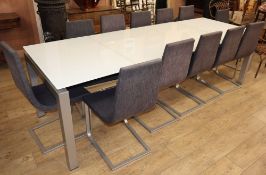 A modern large opaque glass and metal dining table and a set of twelve cloth-upholstered metal