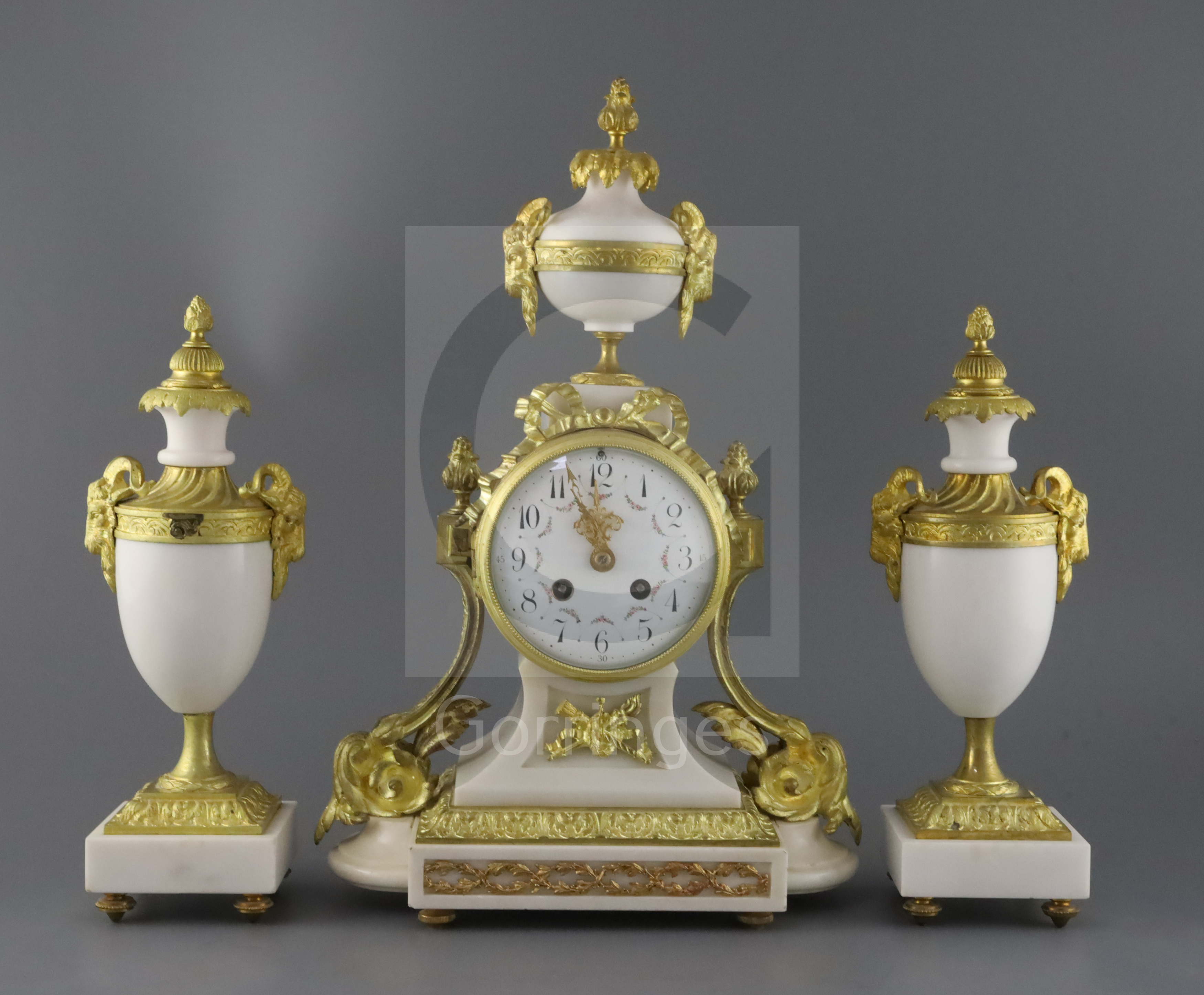 A Louis XVI style ormolu mounted white marble clock garniture, decorated with goat's head motifs,