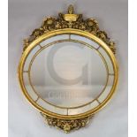 A mid 20th century carved giltwood wall mirror, with urn and scroll surmount, oval marginal plate