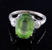 A mid 20th century 9ct white gold and oval cut peridot ring with diamond set shoulders, the