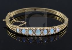 A 20th century pierced gold and graduated seven stone white opal set hinged bracelet, with diamond
