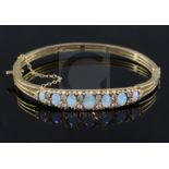 A 20th century pierced gold and graduated seven stone white opal set hinged bracelet, with diamond