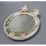A German floral encrusted porcelain wall mirror, surmounted with winged cherubs, overall length