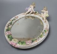 A German floral encrusted porcelain wall mirror, surmounted with winged cherubs, overall length