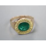 A yellow metal and oval cut foil backed emerald set ring, the milled setting with textured yellow