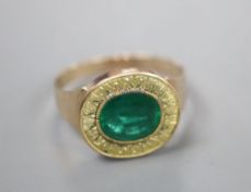 A yellow metal and oval cut foil backed emerald set ring, the milled setting with textured yellow