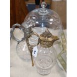 A glass cake stand, a silver plated claret jug and a brass mounted claret jug