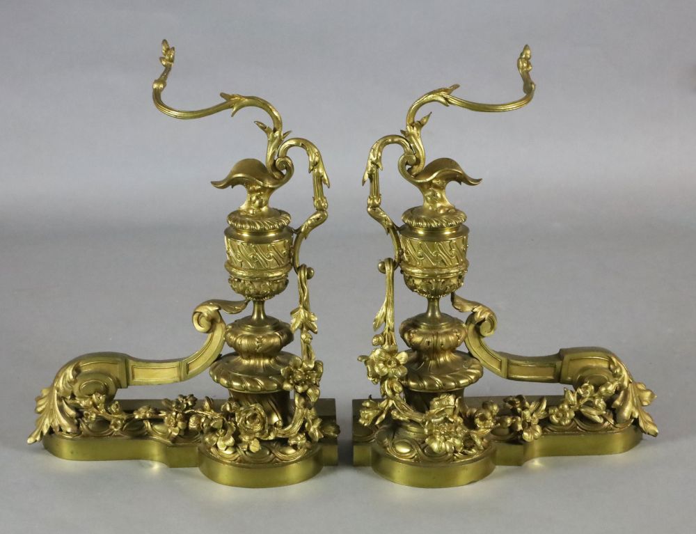 A pair of Louis XVI style ormolu chenets, modelled as urns mounted with scrolling floral foliage,