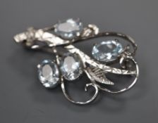 A white metal and four stone aquamarine set scroll brooch, 32mm, gross 4.1 grams.