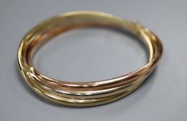 A 9ct three-colour gold bangle of oval, hollow, hinged design with overlapping bands, 18.1g