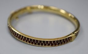 A gilt white metal and twin row red stone set hinged bracelet, with safety chain, gross 22.1 grams.