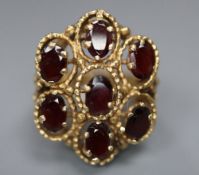 A 14k yellow metal and seven stone garnet set cluster dress ring, size L, gross 11.1 grams.