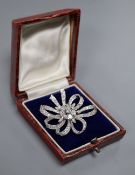 A mid 20th century white metal and diamond cluster set ribbon scroll brooch, set with round and