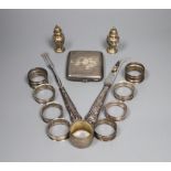 Nine assorted silver napkin rings, a pair of silver pepperettes, a silver cigarette case and pair of