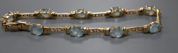 A modern 585 yellow metal and nine stone oval cut blue topaz set bracelet, 21.5cm, gross 16.8