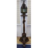 A pierced metal lantern with coloured glass panes, on carved walnut triform pedestal, 206cm overall