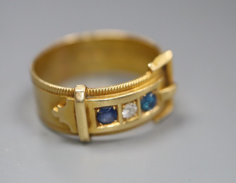 A late Victorian 18ct gold, three stone sapphire and diamond set buckle ring, size O/P, gross 5.1