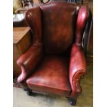 An early 20th century wing back armchair upholstered in burgundy leather on carved claw and ball