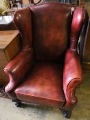 An early 20th century wing back armchair upholstered in burgundy leather on carved claw and ball