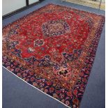 A Mashaed Khorason rug with central medallion and trailing foliate design on a red field, wide