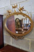 A late Victorian gilt oval wall mirror, surmounted by an urn, flanked by winged griffins, width 70cm