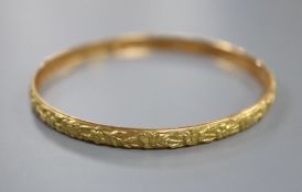 A yellow metal (tests as 18ct) bangle cast with continuous band of flowers, 9g, interior 64mm.