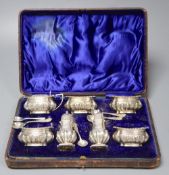 A late Victorian cased silver seven piece condiments set and five spoons (one associated), John