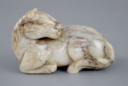 A Chinese white and grey jade figure of a recumbent horse, the stone with some dark brown