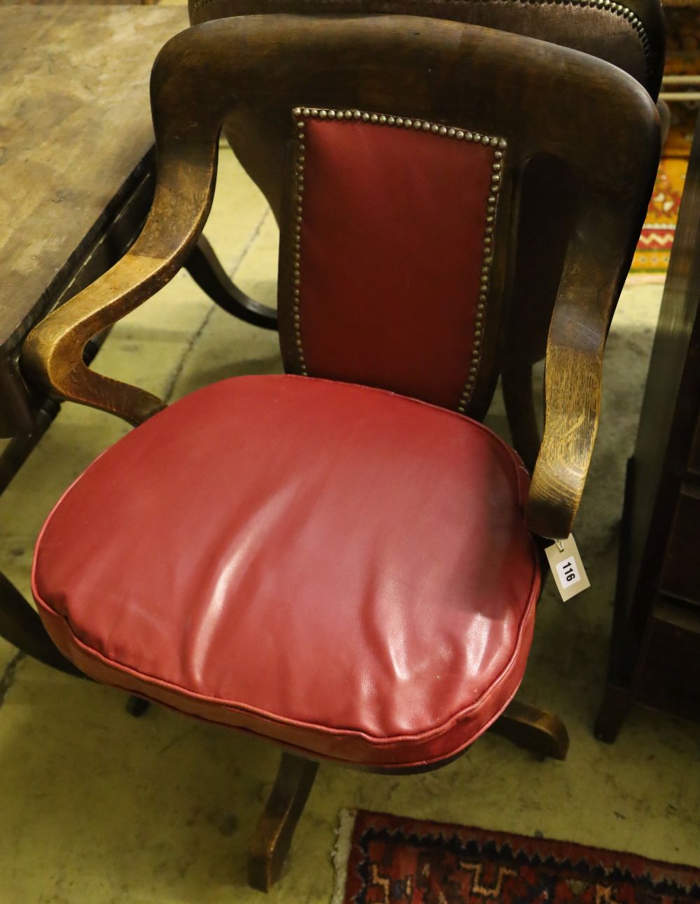A 1920's oak swivel desk chair, the back and seat cushion covered in red hide, width 63cm, depth