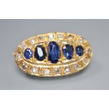 A yellow metal, graduated five stone sapphire and round cut diamond set oval brooch, 28mm, gross 5.8