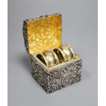 A late Victorian repousse silver serviette ring box, containing two silver gilt serviette rings,