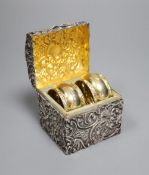 A late Victorian repousse silver serviette ring box, containing two silver gilt serviette rings,