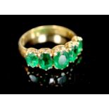 A mid to late 20th century gold and graduated five stone oval cut emerald set half hoop ring, size