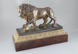 An early 19th century cast iron model of a lion standing with it's foot upon a brass ball, on marble