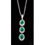 A modern 18ct white gold, emerald and diamond set oval triple cluster drop pendant, on an 18ct white