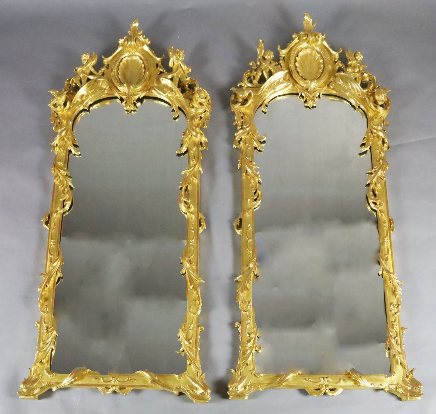 A pair of 19th century French carved giltwood wall mirrors, with scallop and scroll crests flanked
