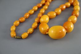 A single strand graduated oval amber bead necklace, 86cm, gross weight 112 grams, with gilt metal