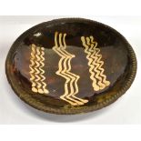 A SLIPWARE DISH WITH CREAM SLIP DECORATION on a dark treacle ground, within crimped border, 34cm