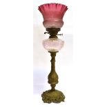 A BRASS BASED OIL LAMP with clear glass reservoir and cranberry glass shade, 67cm high