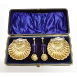 A CASED PAIR OF VICTORIAN SILVER GILT SHELL SALTS AND SPOONS each on three ball feet, the fluted