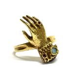 A 9CT GOLD HAND RING set with a small opal and ruby, the front section of a gloved hand to a