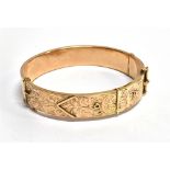 A HALLMARKED 9CT GOLD HINGED BANGLE in the form of a belt and buckle, engraved scroll decoration