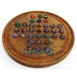 A SOLITAIRE BOARD of turned and painted wooden form, raised on shallow bun feet, 25cm diameter;
